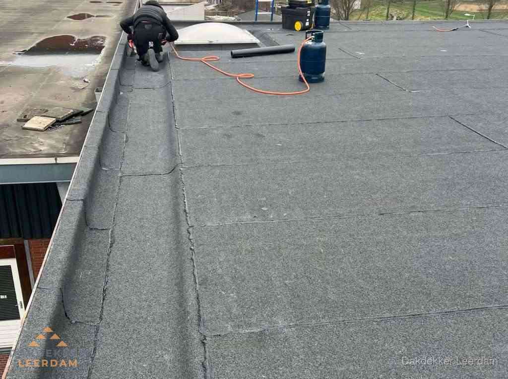 Dakdekker repareert bitumen dakbedekking op groot plat dak in Leerdam